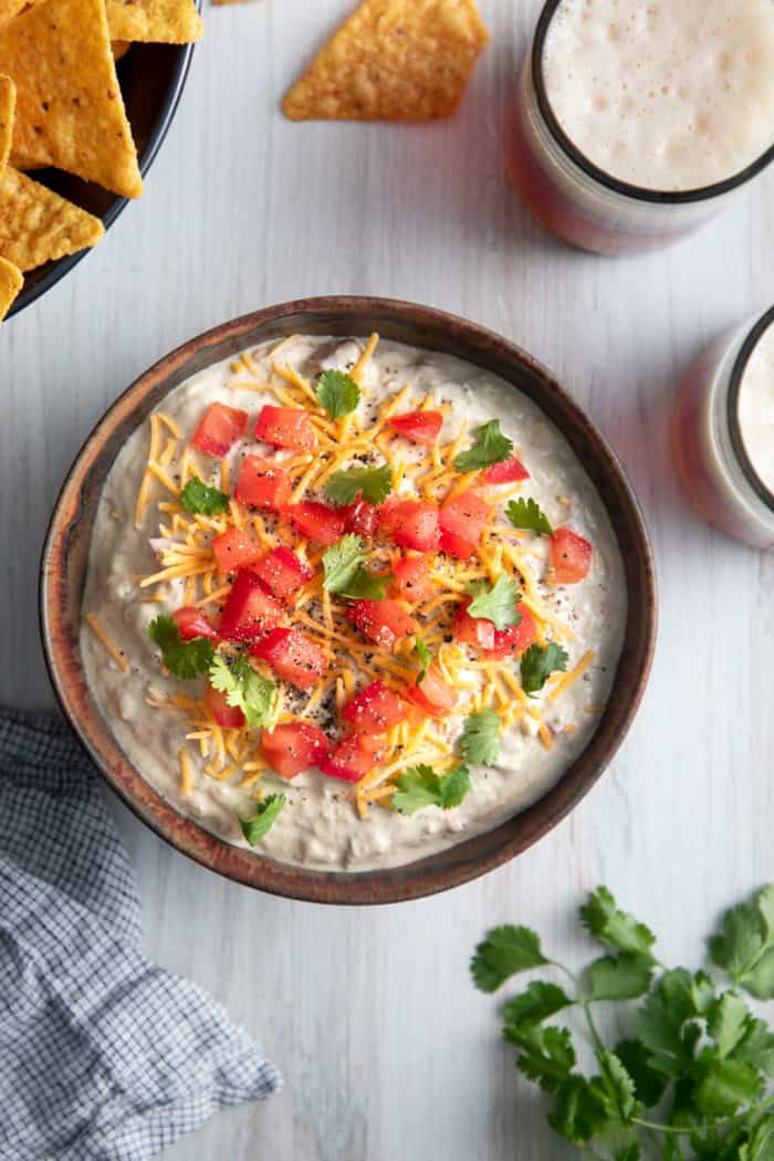 Overhead view of a bowl filled with avocado dip, garnished with shredded cheese, diced tomatoes, and cilantro.