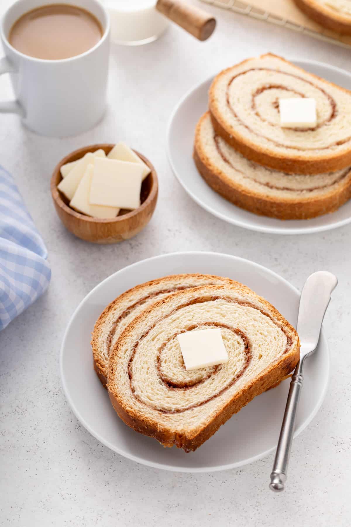 Plate holding two slices of cinnamon swirl bread, with a second plate of bread in the background.