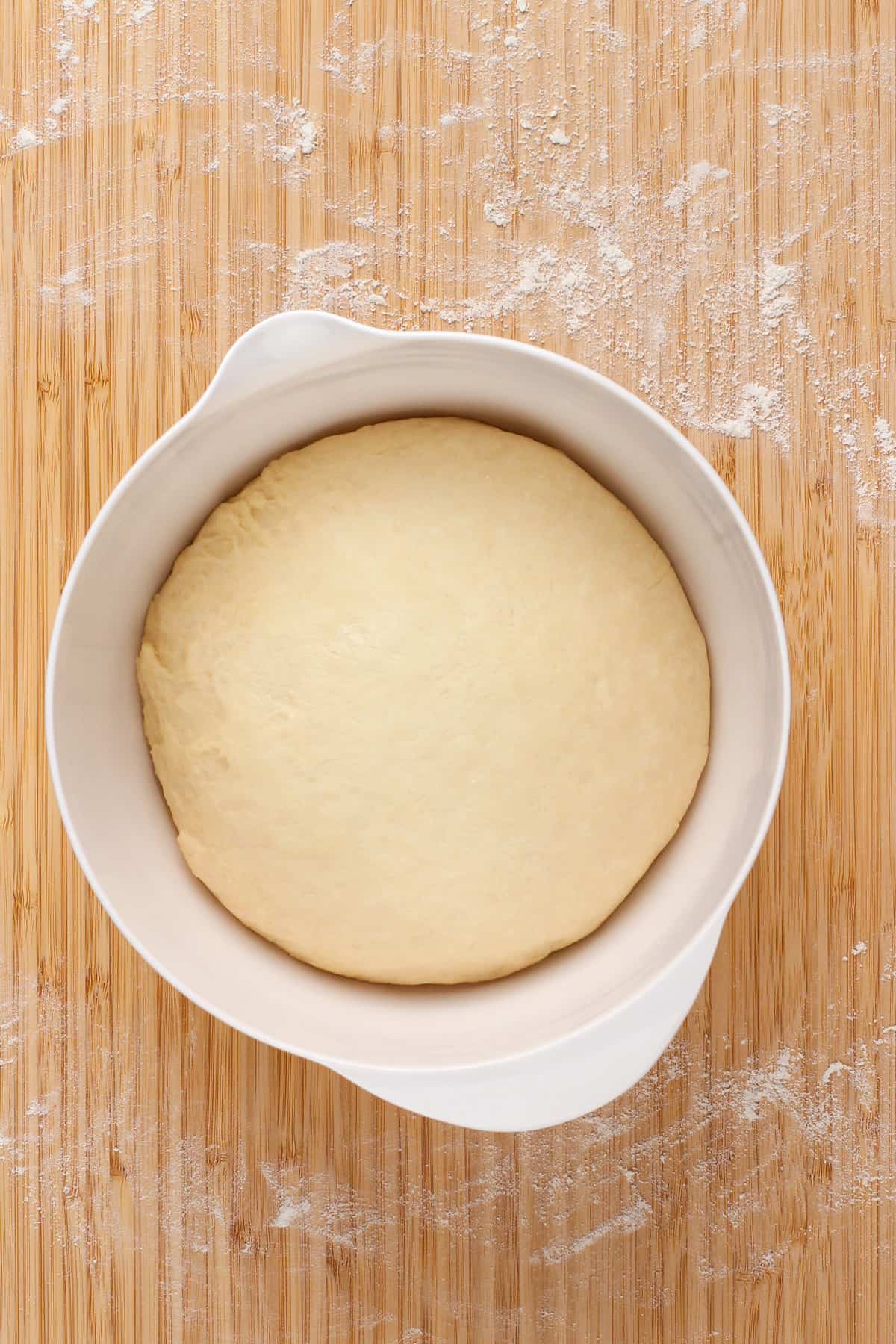 Risen bread dough in a white bowl.