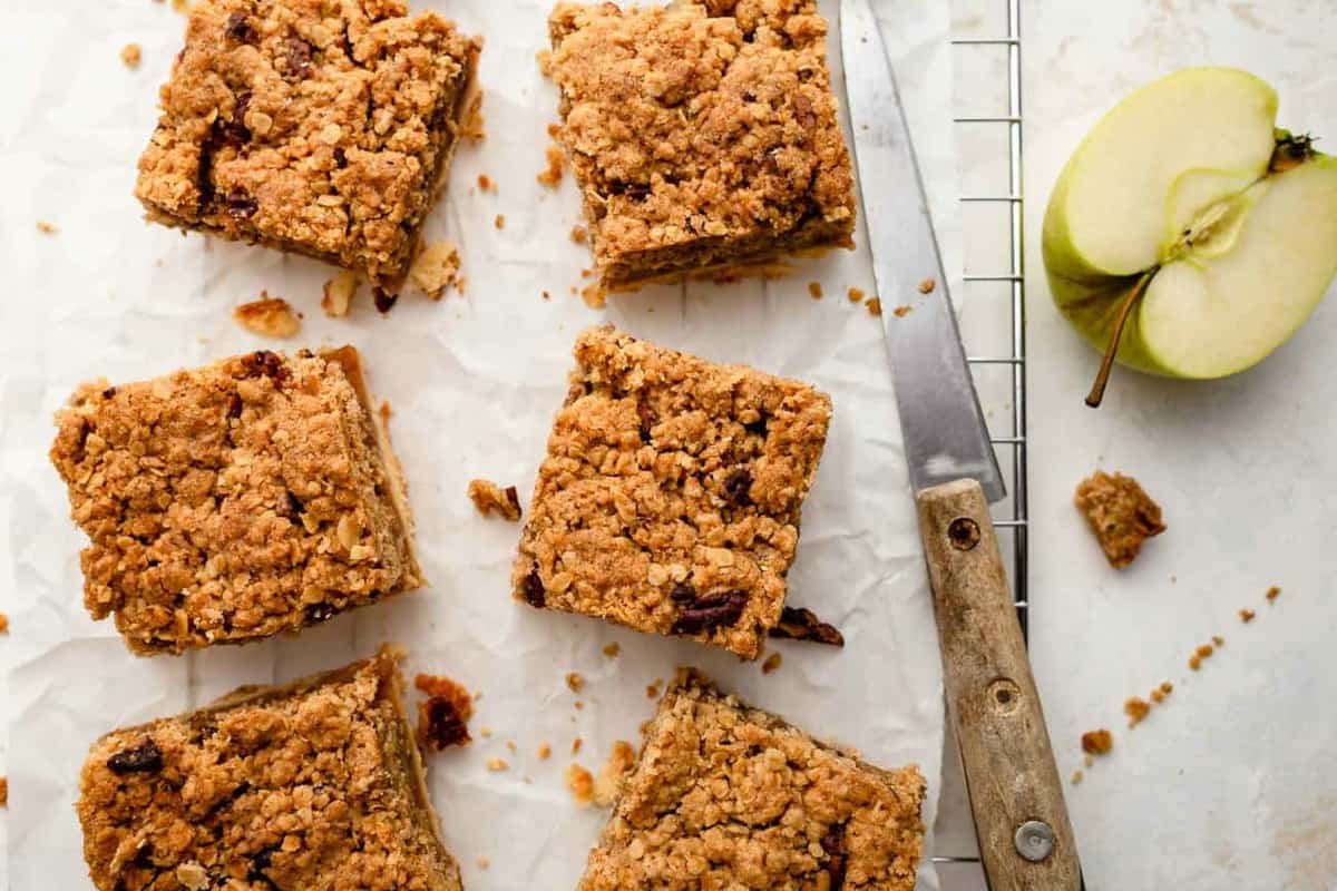 Sliced apple pie bars on parchment paper next to an apple and knife