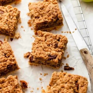 Sliced apple pie bars on parchment paper next to a knife