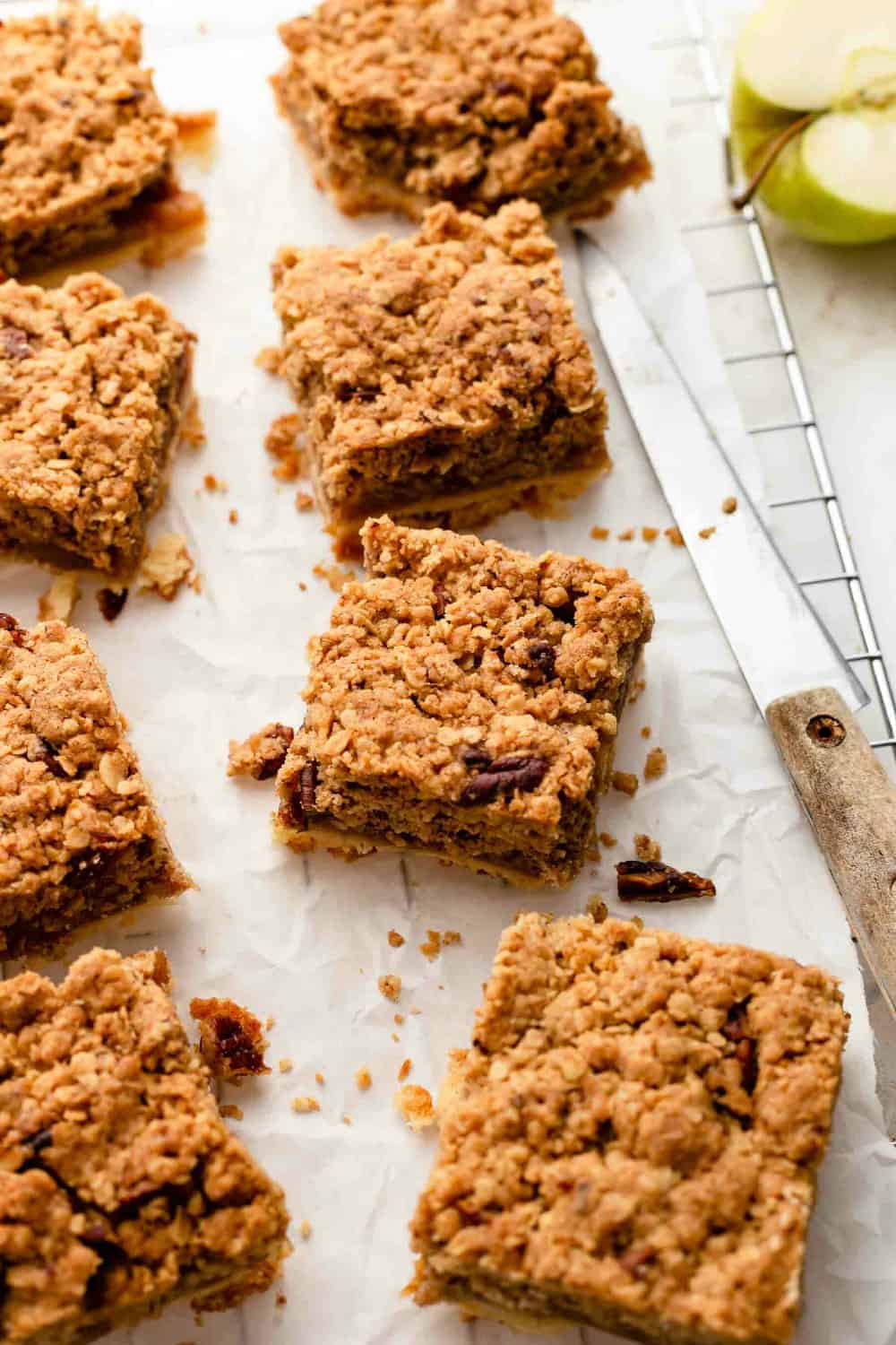 Sliced apple pie bars on parchment paper next to a knife