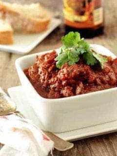 Bowl of prime rib chili next to a spoon on a wooden surface