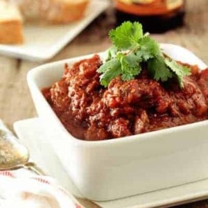 Bowl of prime rib chili next to a spoon on a wooden surface