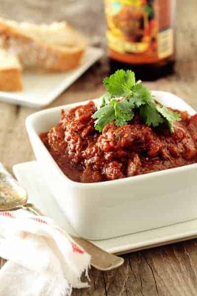 Bowl of prime rib chili next to a spoon on a wooden surface