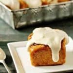 Pumpkin cinnamon roll on a plate in front of a pan of pumpkin cinnamon rolls