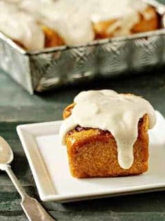 Pumpkin cinnamon roll on a plate in front of a pan of pumpkin cinnamon rolls