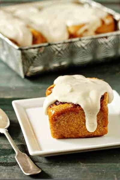 Pumpkin cinnamon roll on a plate in front of a pan of pumpkin cinnamon rolls