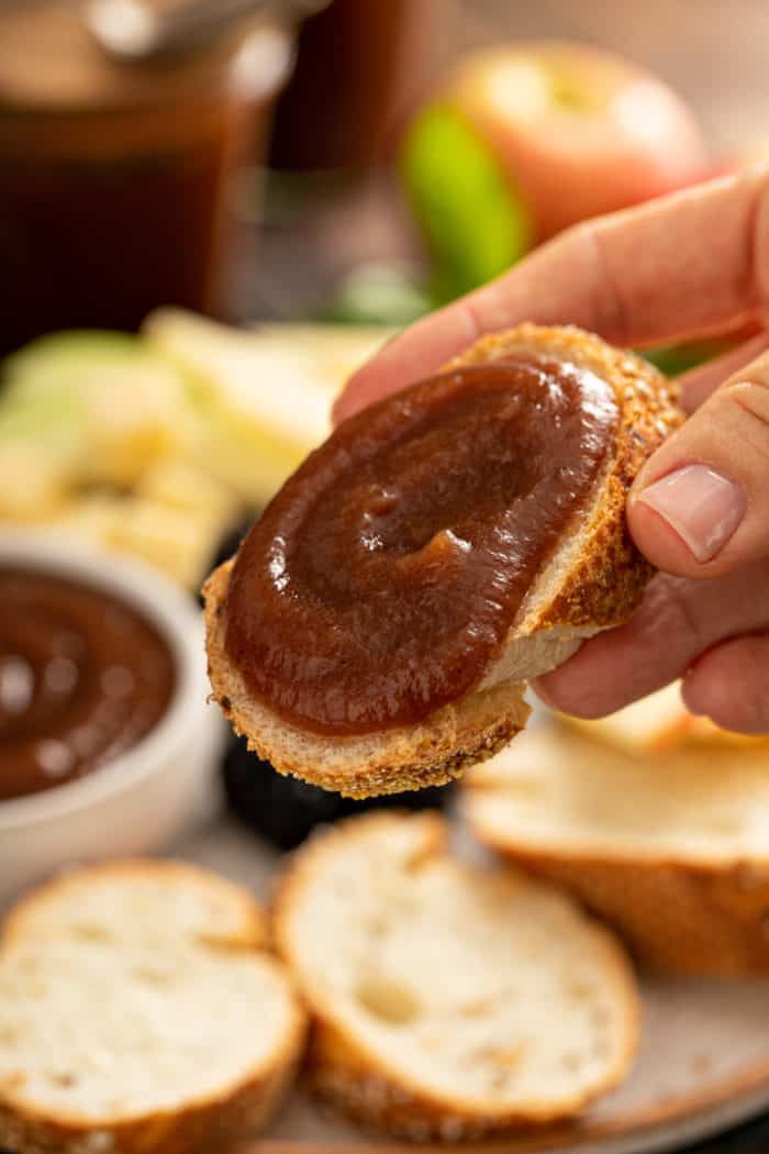 Hand holding up a slice of baguette spread with slow cooker apple butter.