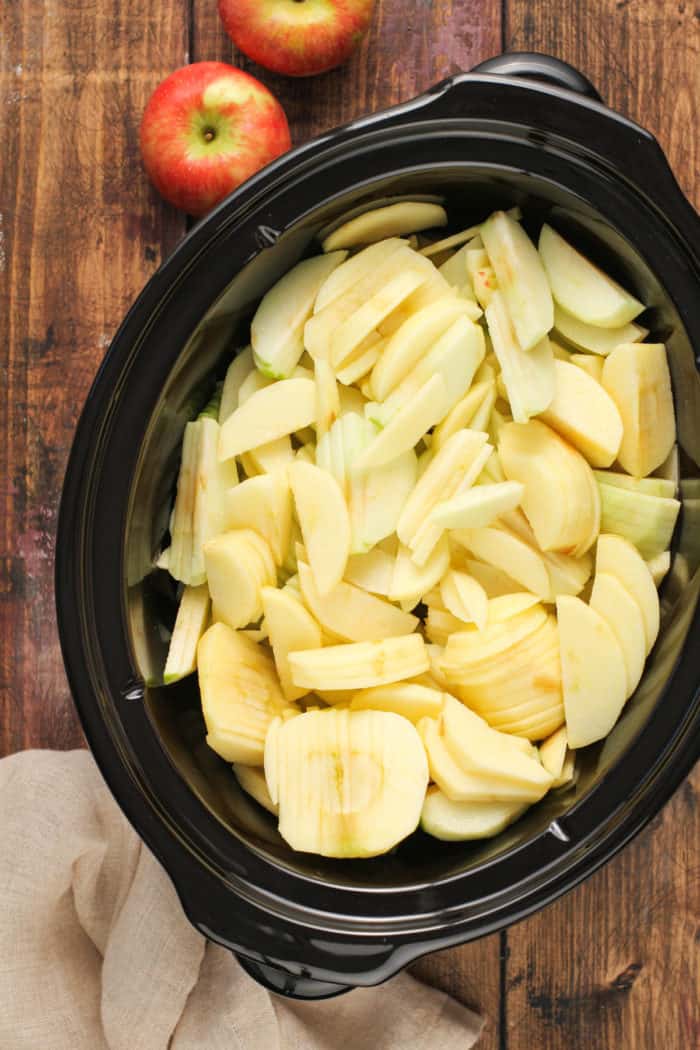 Sliced and peeled apples in the crock of a slow cooker.