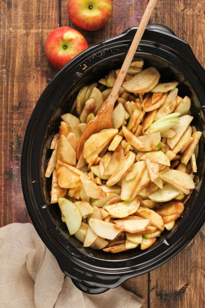 Sliced apples tossed with sugar and spices in the crock of a slow cooker.