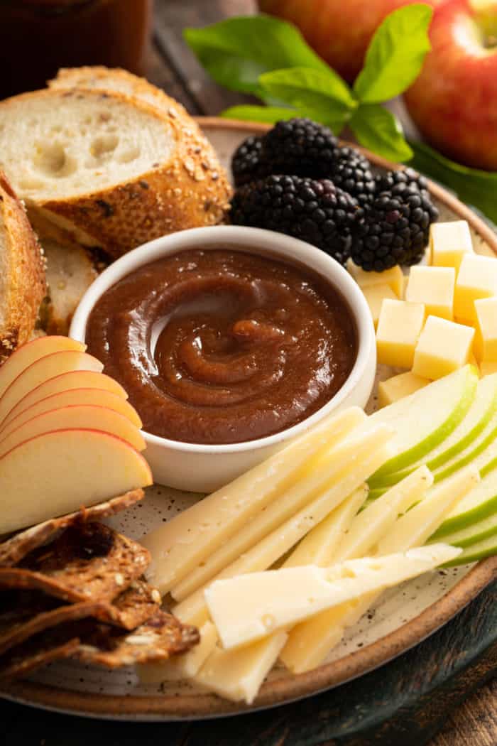 Small bowl of apple butter on a platter, surrounded by sliced apples, cheese, and slices of baguette.