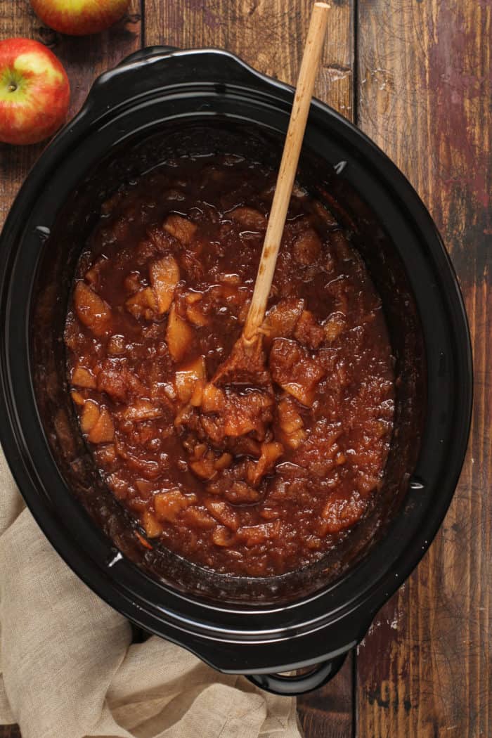 Cooked apples and spices being stirred in the crock of a slow cooker.