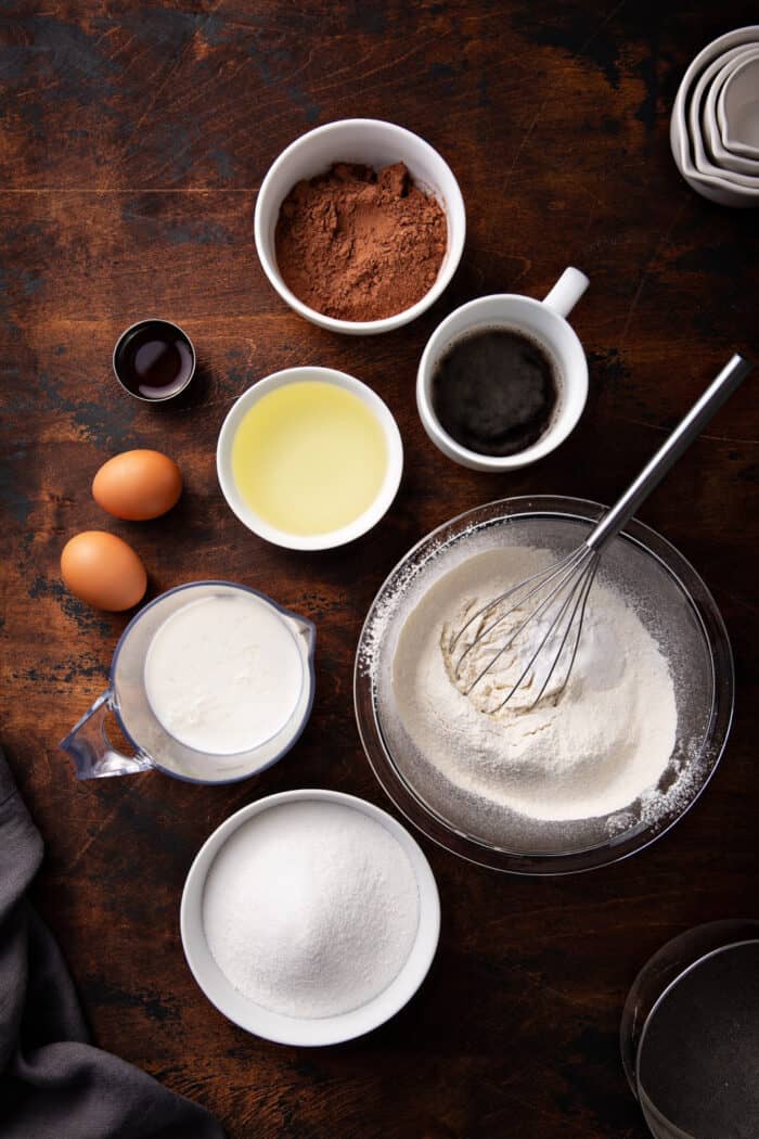 Overhead view of various bowls holding the ingredients for the best chocolate cake recipe on a wooden cutting board