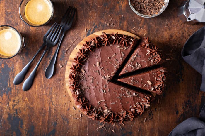 Overhead view of chocolate-frosted cake with 2 slices cut on a wooden cutting board