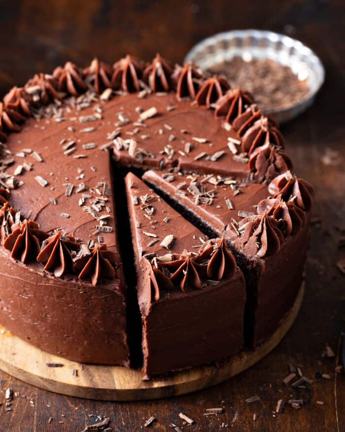 Chocolate cake with chocolate frosting on a wooden cake stand with two slices cut