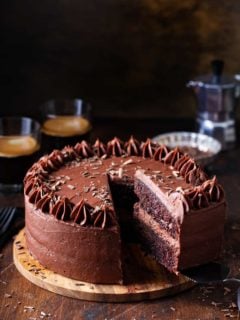 Slice being removed from a double layer chocolate cake with chocolate frosting, with coffee in the background