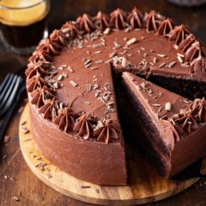 3/4 view of chocolate cake with chocolate frosting on a wooden cake stand with a slice being removed