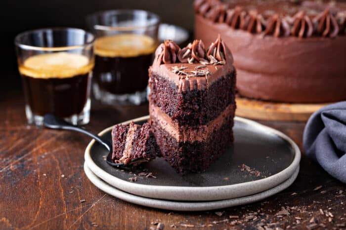 Slice of double-layer chocolate cake with chocolate frosting on a gray plate with a fork taking a bite out of the cake