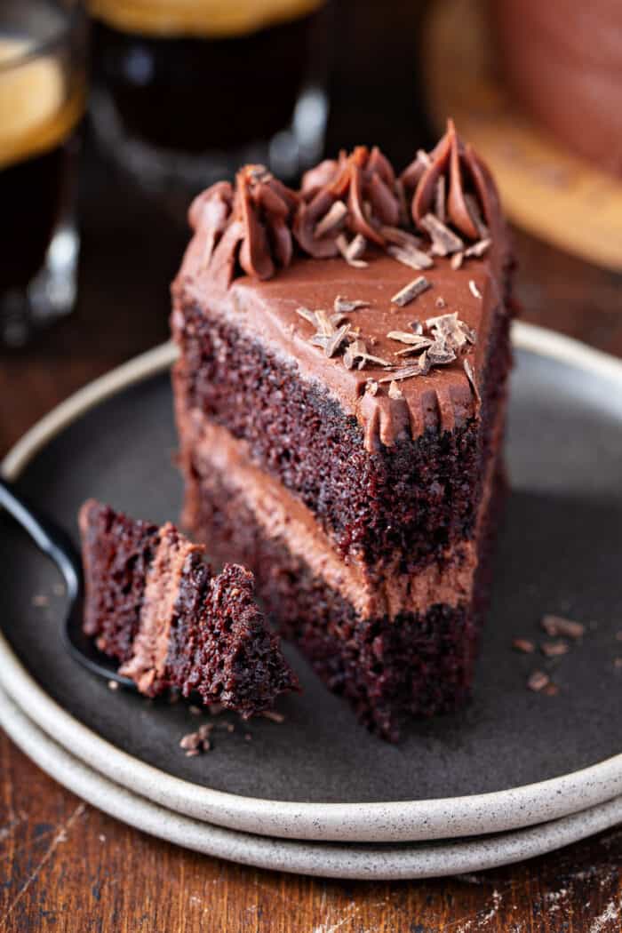 Fork taking a bite out of a slice of chocolate-frosted chocolate cake on a gray plate