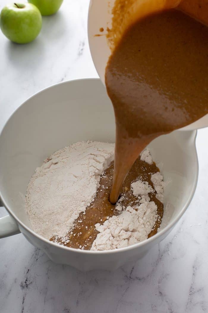 Wet ingredients for apple cinnamon muffins being poured on top of dry ingredients in a white mixing bowl