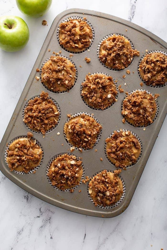 Apple cinnamon muffin batter topped with streusel topping in a muffin tin, ready to be baked