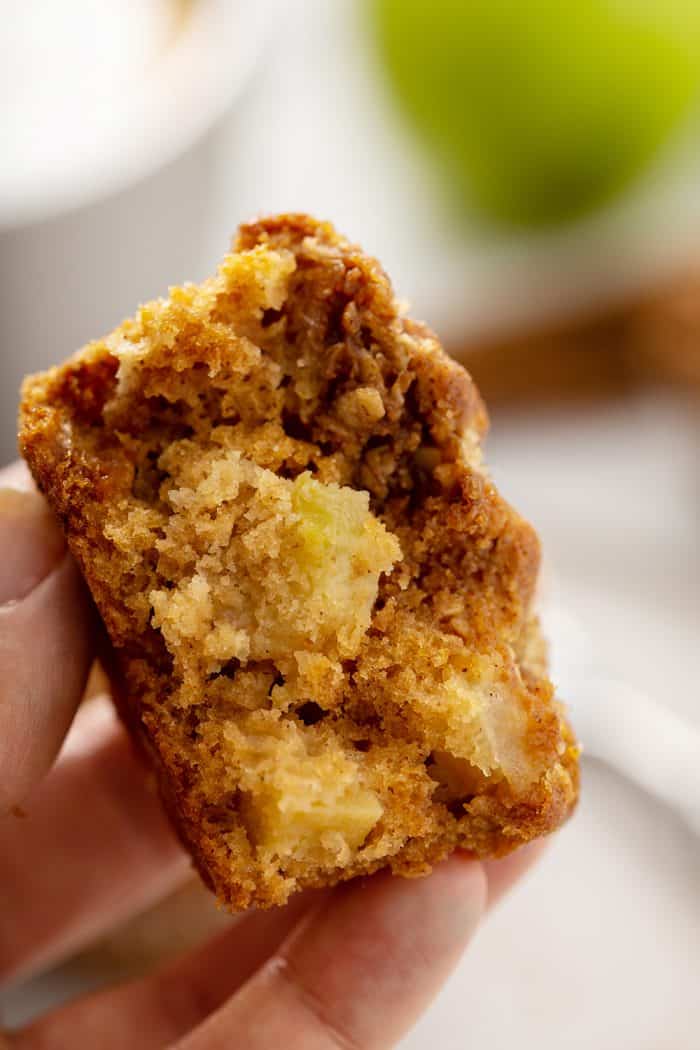 Hand holding up half of an apple cinnamon muffin to show big pieces of apple in the muffin
