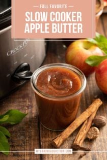 Open glass jar of apple butter set next to a slow cooker on a wooden tabletop. Text overlay includes recipe name.