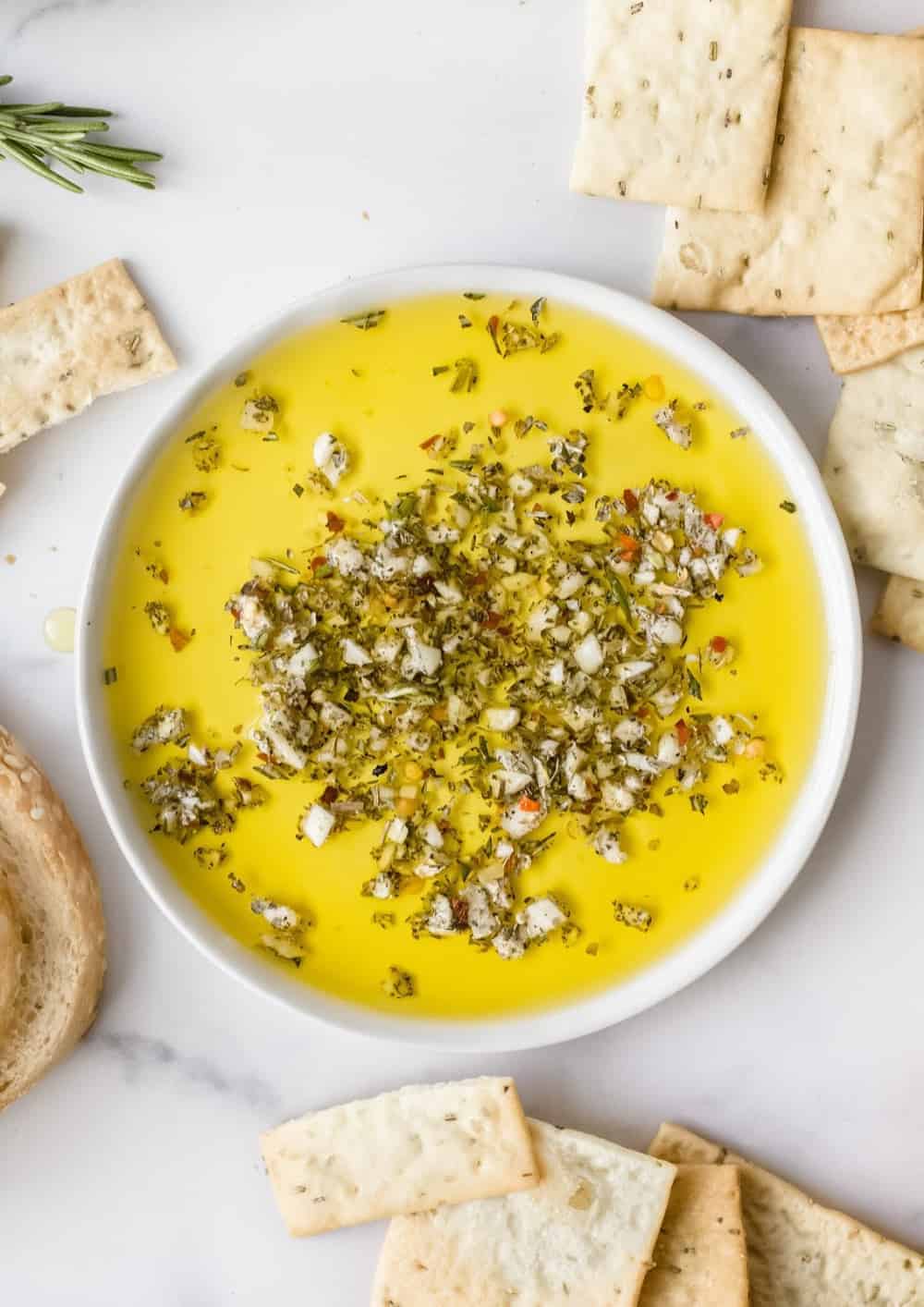 Shallow white bowl filled with olive oil herb dip on a white surface