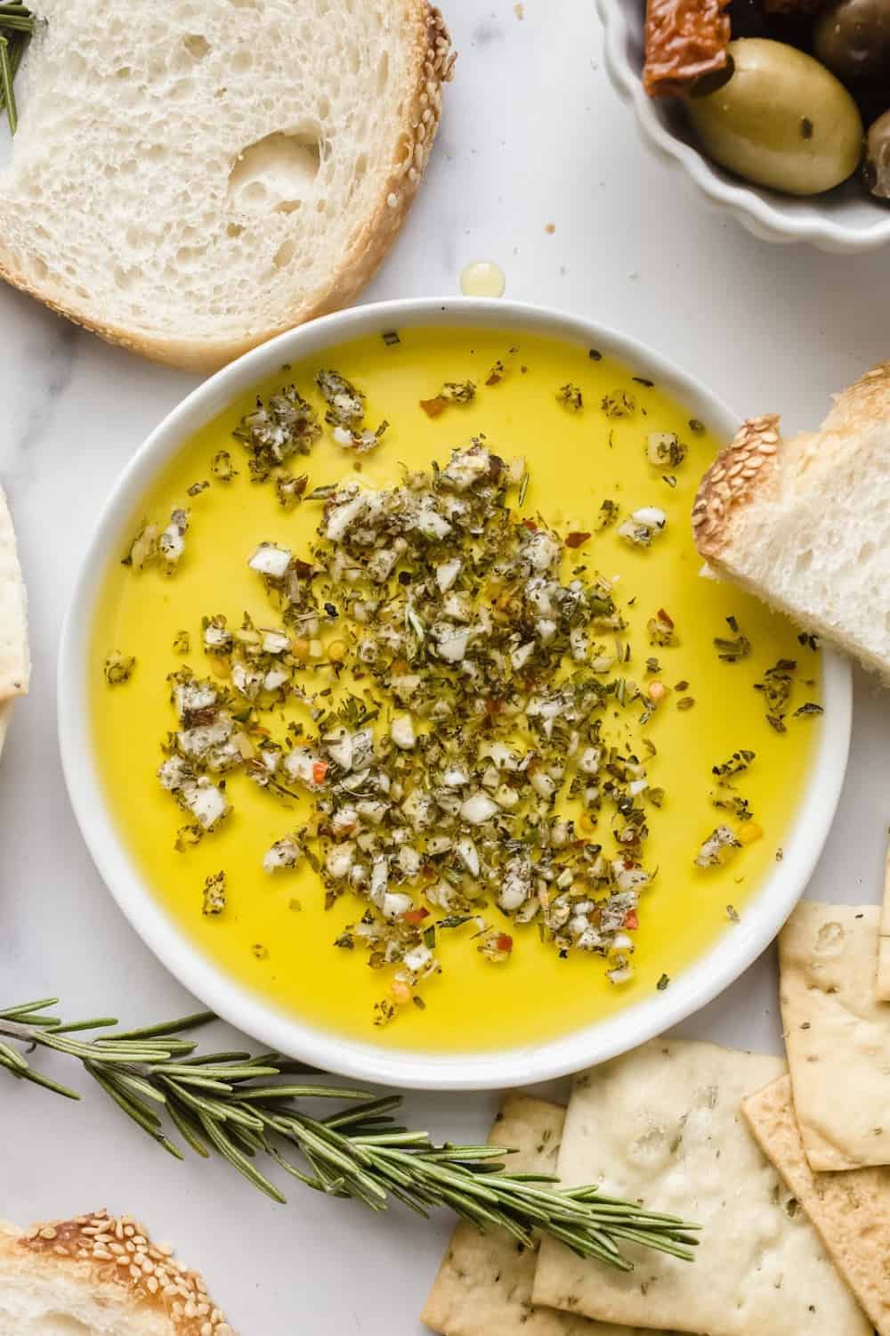 Close up of a bowl with olive oil herb dip next to bread and fresh rosemary