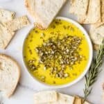 Bread and crackers surrounding a white bowl of olive oil herb dip