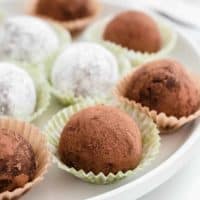 Rum balls coated in both cocoa powder and powdered sugar arranged on a plate