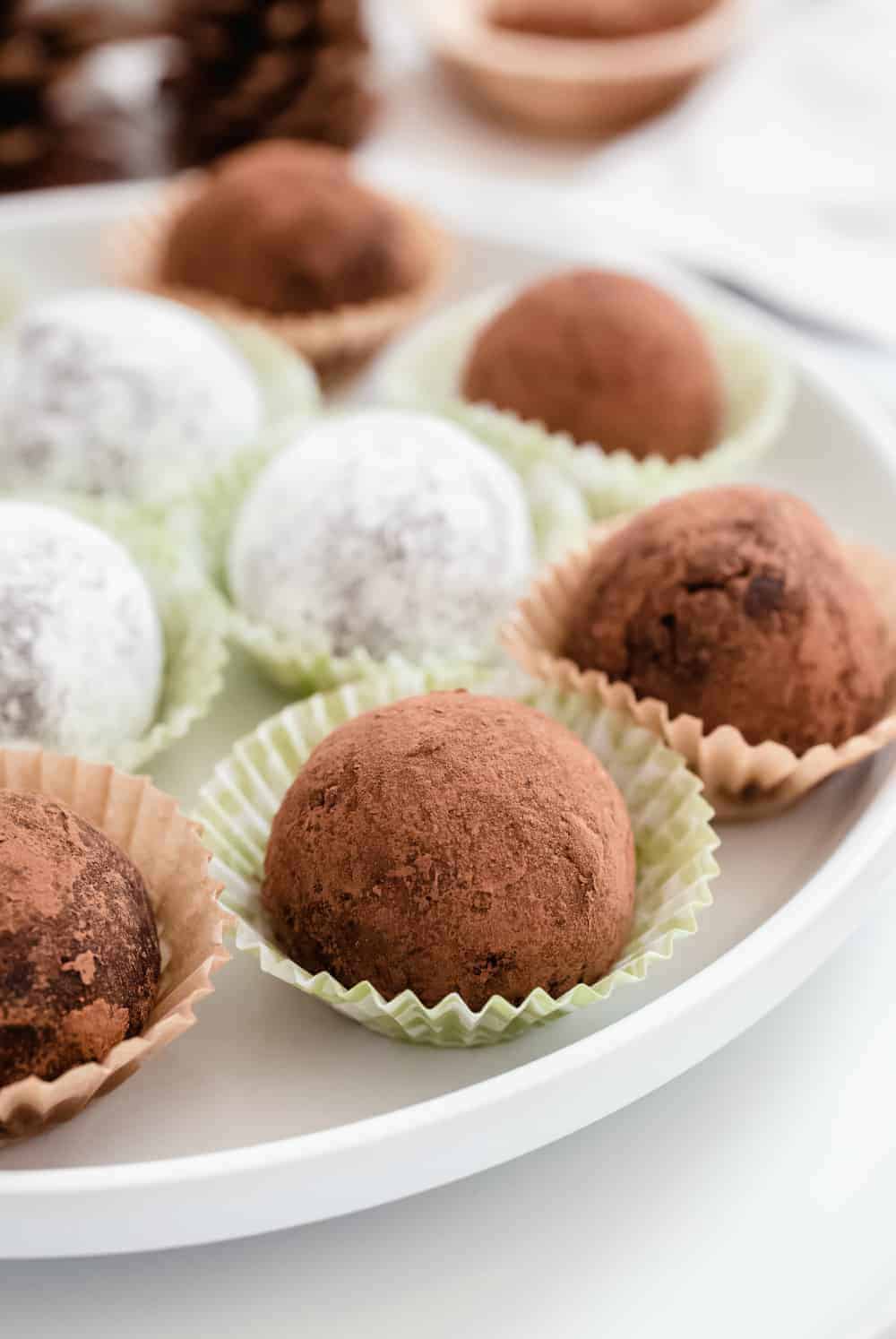 Rum balls coated in both cocoa powder and powdered sugar arranged on a plate