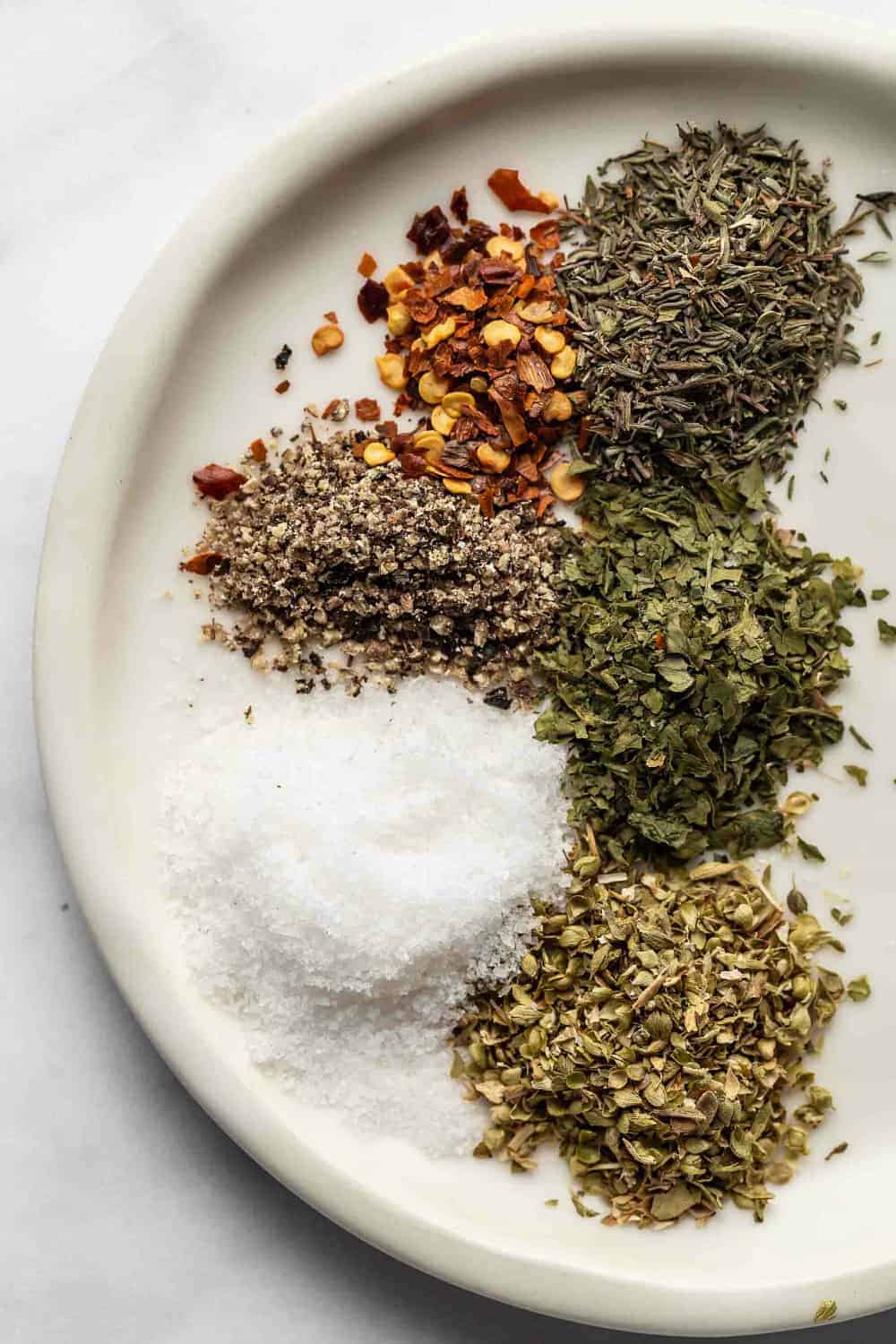 Herbs and spices for sausage and lentil soup on a white plate