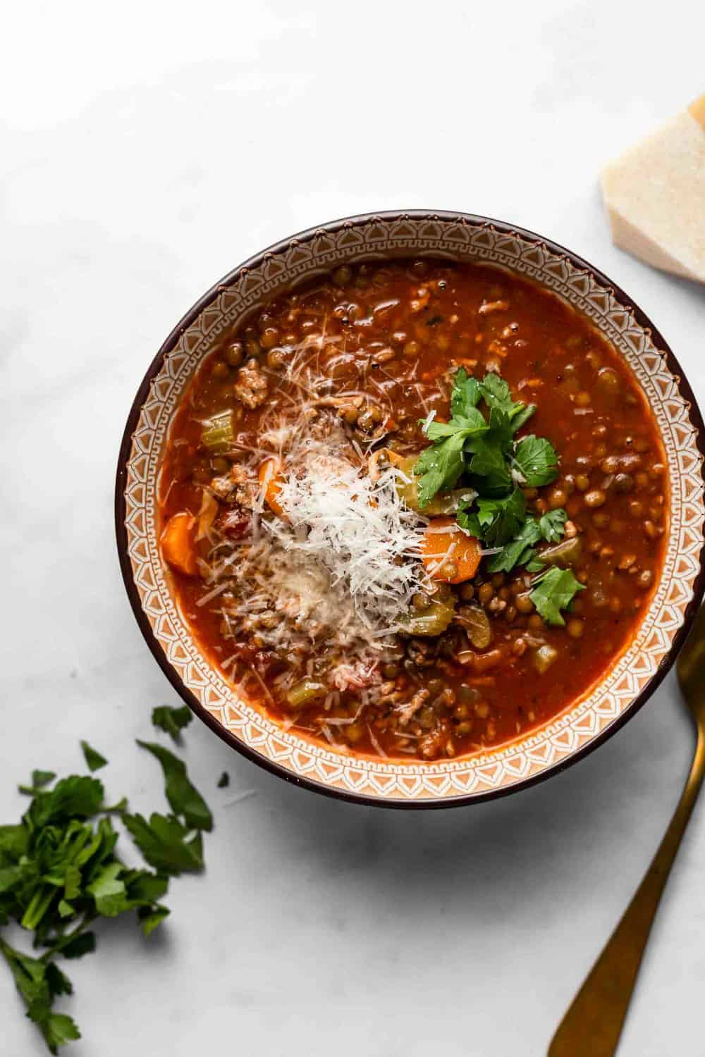 Bowl of sausage and lentil soup next to a spoon and chopped parsley