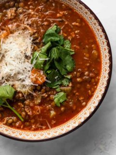 Close up of a bowl of sausage and lentil soup garnished with herbs and parmesan cheese
