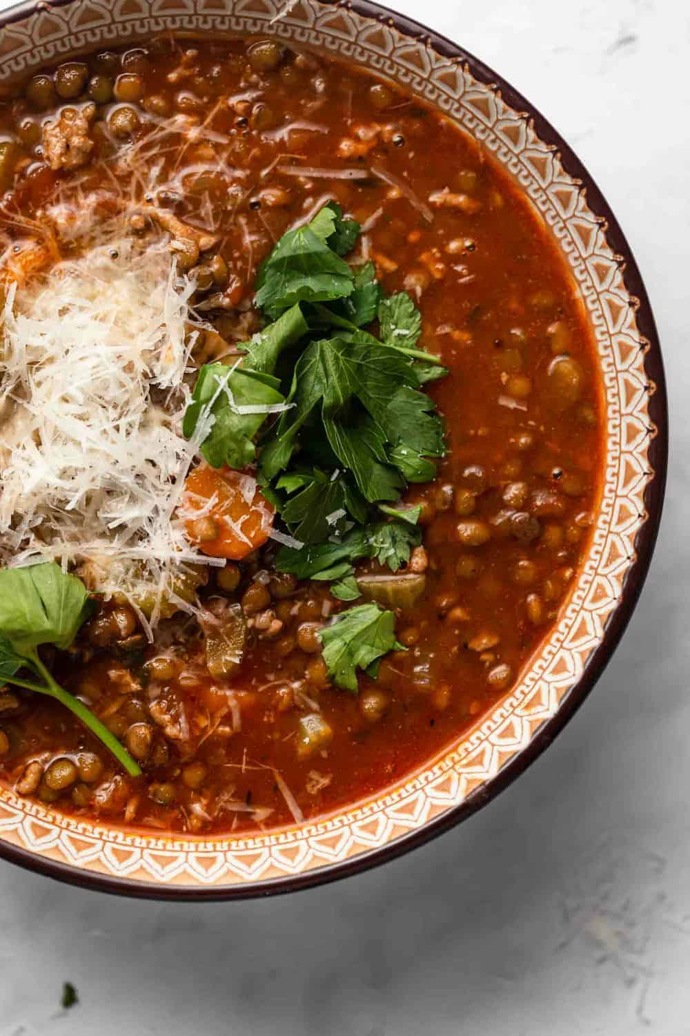 Close up of a bowl of sausage and lentil soup garnished with herbs and parmesan cheese