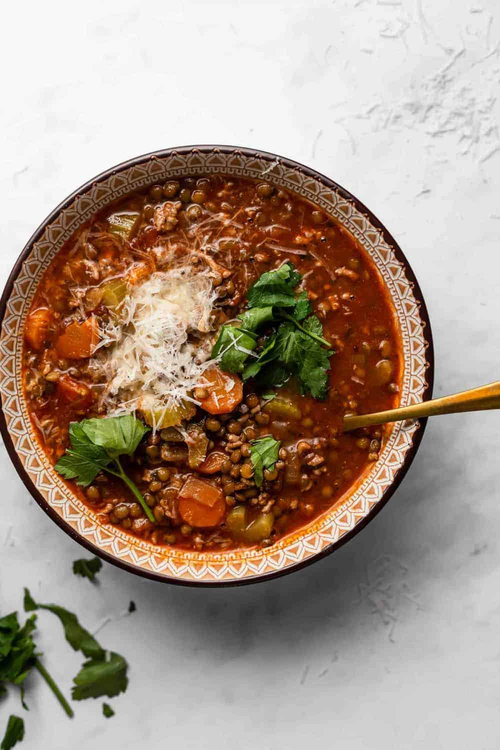 Overhead of a spoon in a bowl of sausage and lentil soup on a white surface