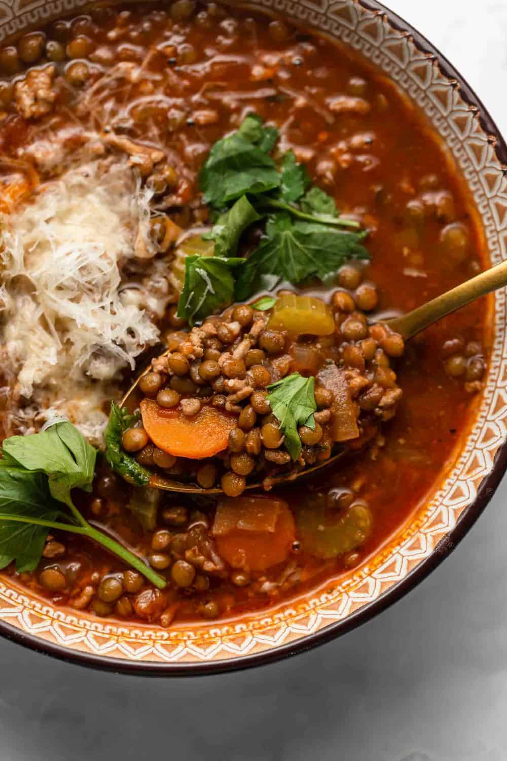 Spoon holding a spoonful of sausage and lentil soup over a bowl of the soup