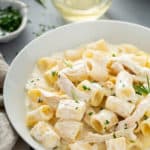 White pasta bowl with goat cheese pasta with shredded chicken and rosemary, garnished with chopped parsley