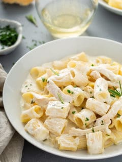 White pasta bowl with goat cheese pasta with shredded chicken and rosemary, garnished with chopped parsley