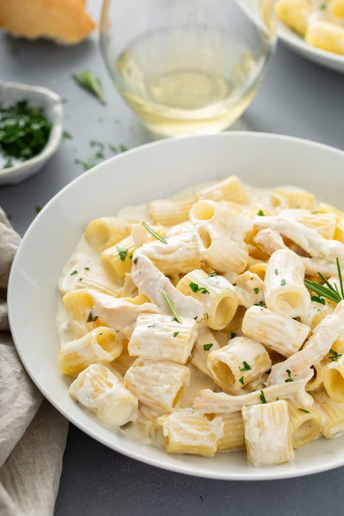 White pasta bowl with goat cheese pasta with shredded chicken and rosemary, garnished with chopped parsley