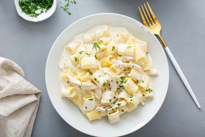 Overhead view of goat cheese pasta in a white pasta bowl alongside a gold fork