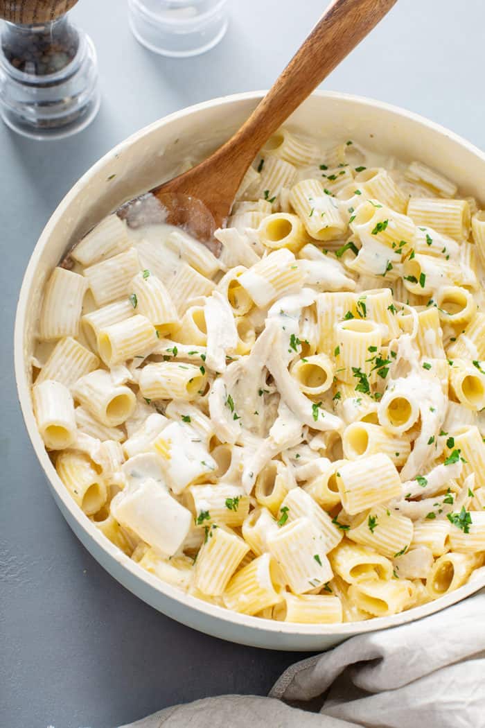 Goat cheese pasta sauce with chicken being combined with cooked rigatoni pasta in a large saucepan