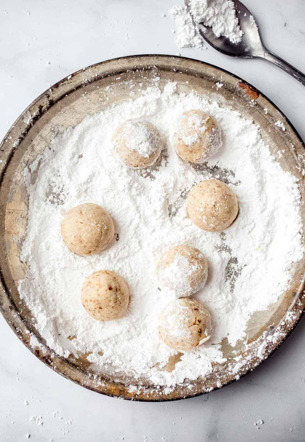 Freshly baked snowball cookies being rolled in powdered sugar