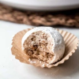 Close up of a snowball cookie with a bite taken out of it on a paper liner