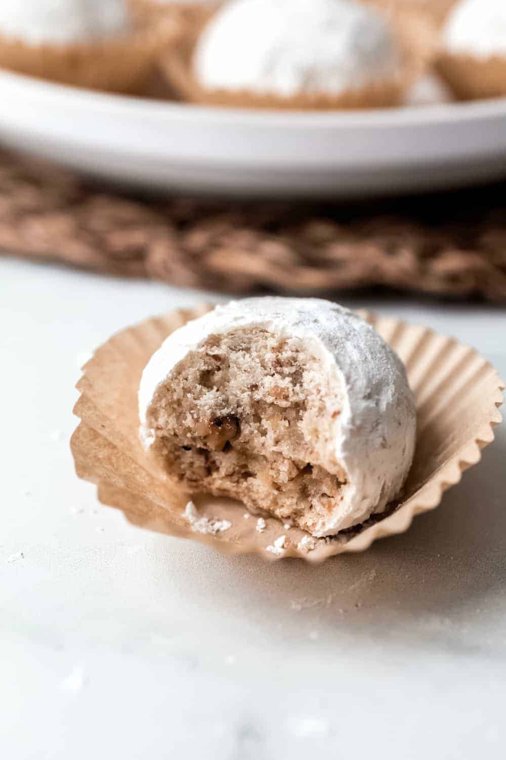 Close up of a snowball cookie with a bite taken out of it on a paper liner