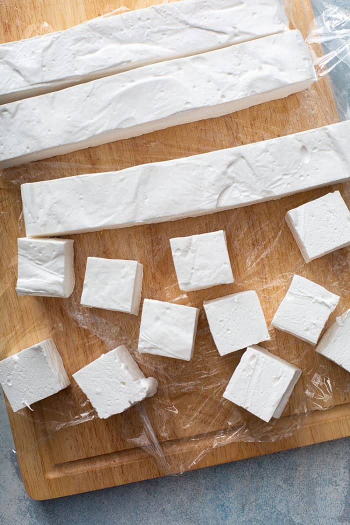 Homemade marshmallows being sliced on a wooden cutting board