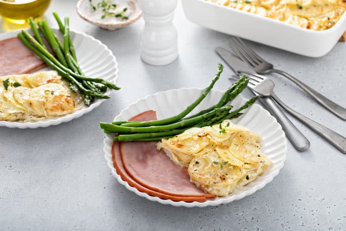 White plates on a dinner table filled with ham, asparagus, and scalloped potatoes