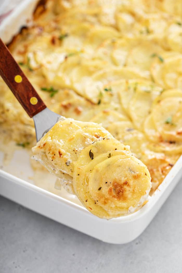 Spatula serving up a portion of scalloped potatoes from a casserole dish